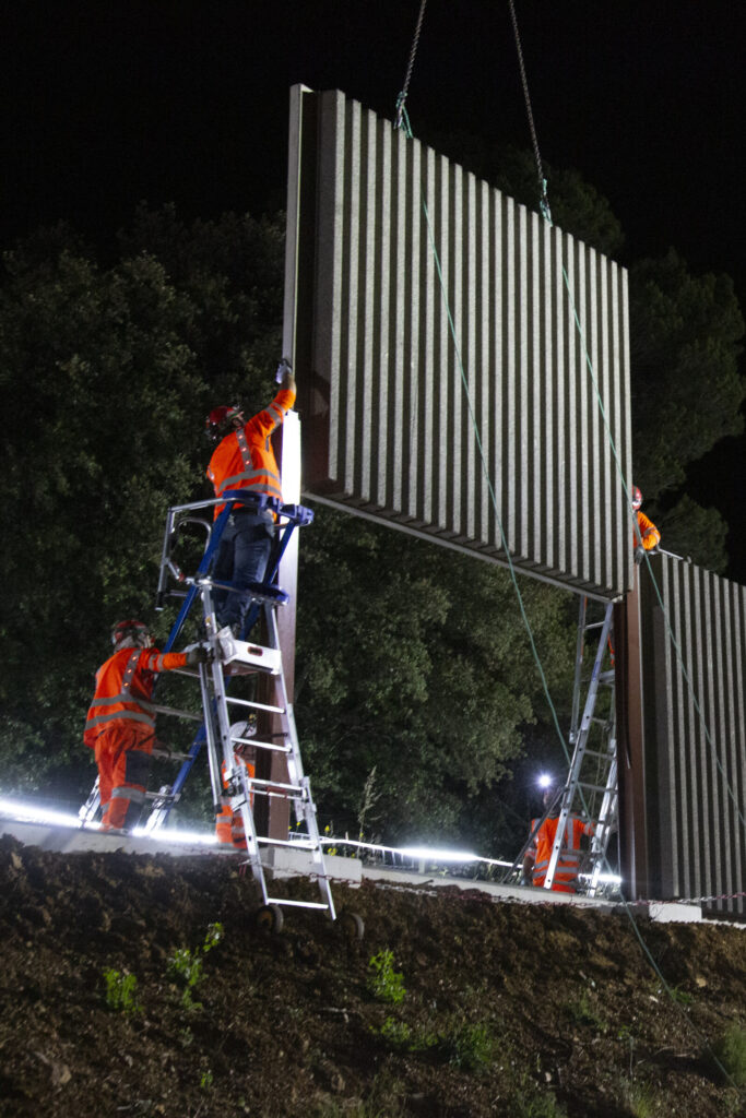 Chantier de nuit dans le Var : des ouvriers sur escabeaux guident la pose d’un écran acoustique suspendu à une grue (AER, réseau Escota)